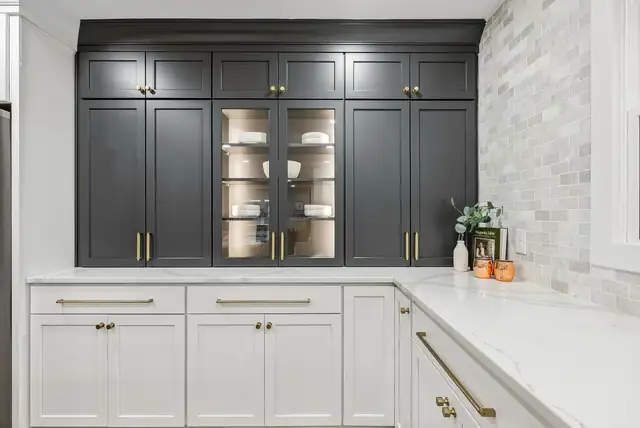Columbus kitchen with charcoal glass-front upper cabinets, white lowers with brass pulls and a marble tile backsplash