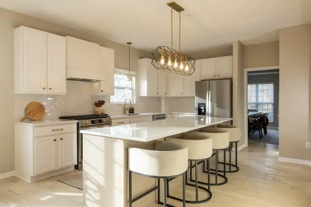 Dublin kitchen with a peninsula, cream upholstered counter stools, a brass linear chandelier and white shaker cabinets