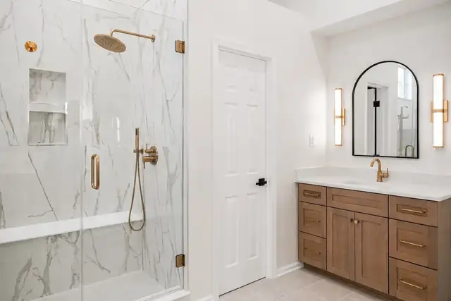 Dublin, OH primary bathroom remodel with marble-look tile shower, wood vanity with gold pulls, arched mirror and brass sconces