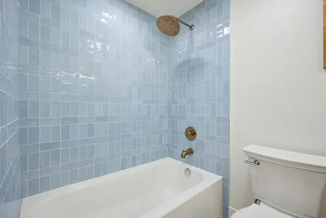 Upper Arlington, OH kids' bath with light blue tile tub surround and brass shower fixtures