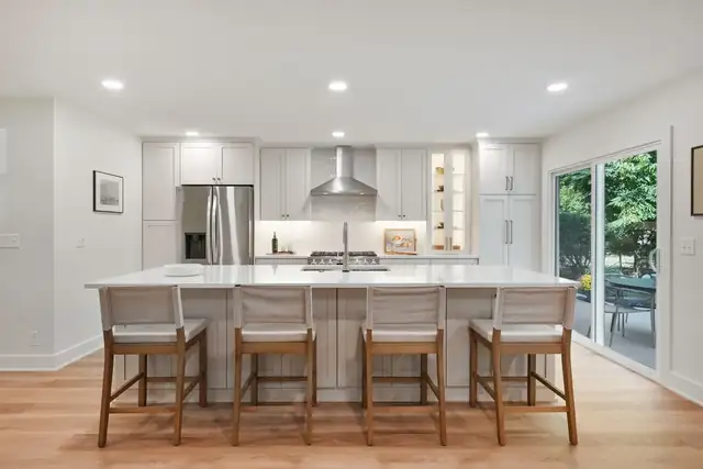 Upper Arlington, OH kitchen remodel with large white island and wood stools, stainless refrigerator and sliding door to the yard