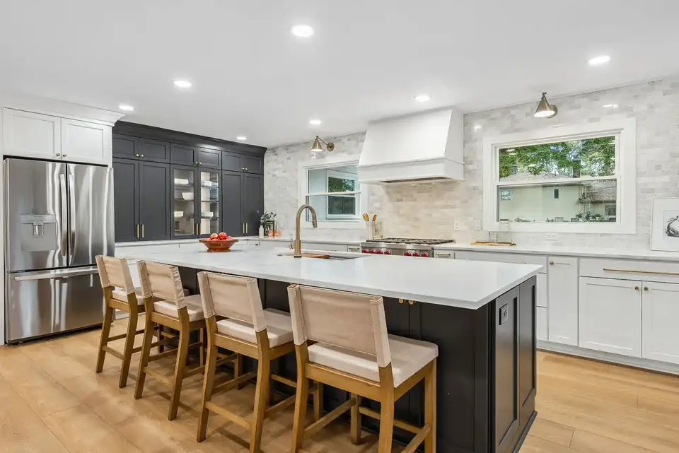 Kitchen remodeling Columbus Ohio project in Upper Arlington: long white quartz island with woven stools, charcoal pantry cabinets, white range hood and white oak floors