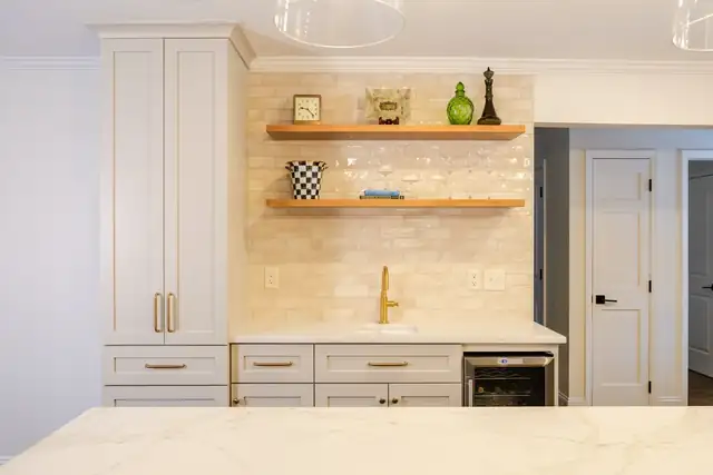 Upper Arlington, OH wet bar with white custom cabinets, marble-look counter, brass faucet, floating wood shelves and wine cooler